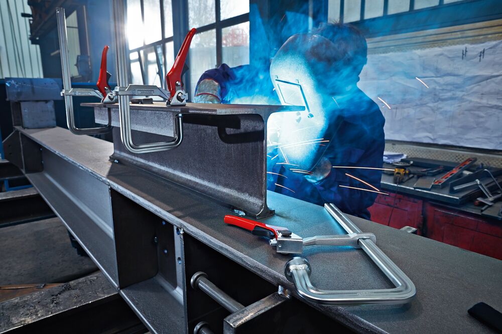 Le serre-joint GUH serre les poutres en acier et l'ouvrier procède au soudage