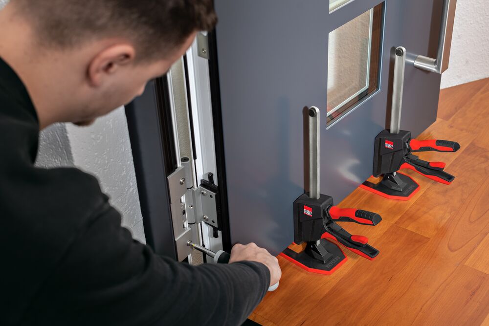 L'outil de montage à une main BEYCEPS soulève une porte d'entrée, le technicien ajuste correctement la porte à l'aide d'un tournevis
